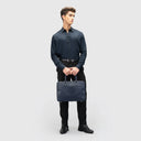 Man in navy blue lyocell shirt with full sleeves, sleek finish, button loops, paired with black pants, holding a bag.