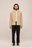 Man wearing beige suede leather jacket with horn buttons, full sleeves and flap pockets, paired with black pants and loafers.