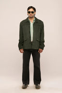 Man wearing dark green suede leather jacket with horn buttons, flap patch pockets, and full sleeves, styled with black pants.