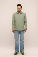 Man wearing sage green linen shirt with relaxed fit and full sleeves, paired with jeans and sneakers.