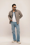 Man in a full-sleeve grey shirt jacket for men featuring silver snap buttons and pocket, paired with jeans and sunglasses.