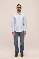 Man in light blue chambray shirt for men with full sleeves, jetted pockets and apple-cut hem, paired with jeans.