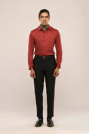 A man wearing a rust red lyocell shirt with a glossy finish and black pants, showcasing full sleeves and unique button loop details.