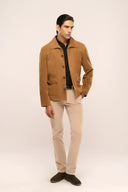 Man wearing brown suede leather jacket with full sleeves, horn buttons, spacious flap pockets, paired with beige pants.