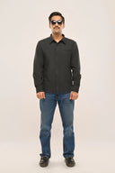 A man wearing a charcoal black chambray shirt with jetted pocket and loop closure, paired with blue jeans.