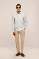 Man wearing light blue linen shirt with full sleeves and apple-cut hem, paired with beige pants, sunglasses and loafers.