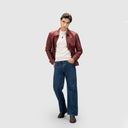 Man wearing rust red leather jacket for men in a regular fit, featuring zip closures, with a white t-shirt and blue jeans