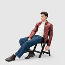 Person wearing a rust red leather jacket for men, blue jeans and white tee, sitting on a chair against a white background