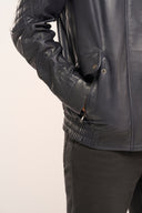 Close-up of man wearing navy blue lamb nappa leather jacket, featuring flap and slip-in pockets with zipper and elasticated hem.