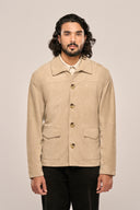 Close-up of man in beige suede leather jacket with horn buttons, full sleeves and flap pockets, paired with black pants.