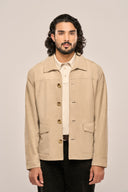 Man in beige suede leather jacket close-up view, with horn buttons, full sleeves and flap pockets, paired with black pants.