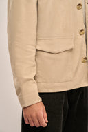 Close-up side view of man in beige suede leather jacket featuring full sleeves, horn buttons, and flap pockets.