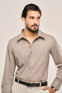 Close up front view of man in gray pleat shirt with full sleeves, paired with light pants and black belt.