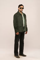 Man wearing dark green suede jacket side profile with full sleeves, patch pockets, and horn buttons, worn with black pants.