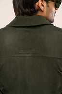 Close-up back view of man in dark green suede leather jacket featuring collar and ​​TZÁR logo patch.