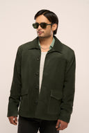 Close-up of man wearing suede leather jacket in dark green featuring patch pockets, collar, horn buttons, and full sleeves.