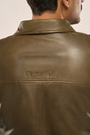 Close-up back view of man wearing dark olive leather jacket for men, featuring structured back panel and TZÁR logo patch