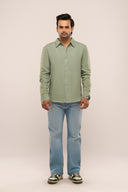 Man wearing sage green linen shirt with relaxed fit and full sleeves, paired with jeans and sneakers.