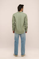 Back view of man in sage green linen shirt showing relaxed silhouette, full sleeves, and apple-cut hem, paired with jeans.
