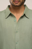 Close-up of man wearing sage green linen shirt highlighting breathable weave and collar.