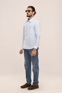 Side view of a man in a light blue chambray shirt showing full sleeves and tailored relaxed fit, paired with jeans.