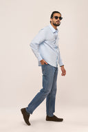 Light blue relaxed-fit chambray shirt for men with full sleeves and apple-cut hem, paired with jeans and sunglasses.