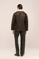 Back view of man in distressed brown leather jacket for men with unique stitch detailing and fur collar, and leather pants.