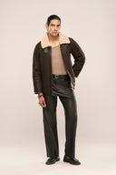 Man wearing brown leather jacket for men with fur lining, full sleeves and zip front, paired with leather pants.