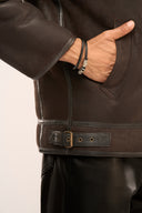Close-up of man wearing distressed brown leather jacket featuring full sleeves, slip-in pockets, and side seam buckles.