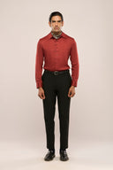 A man wearing a rust red lyocell shirt with a glossy finish and black pants, showcasing full sleeves and unique button loop details.
