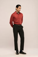 A man dressed in a slim-fit, sleek rust red shirt with full sleeves and button loops, complemented by black pants, side view.
