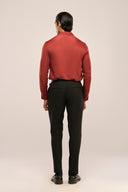 Man's back view in a slim-fit rust red shirt for men with glossy finish and full sleeves, paired with black pants and shoes.