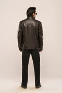 Man wearing black leather jacket, structured back panel, full sleeves with zipper, TZÁR logo patch, black pants, back view