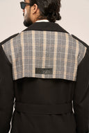 Man in black trench coat featuring plaid accent, TZÁR leather label detail, and waist belt, shot from behind.