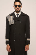Man in black trench coat with plaid detail on shoulders and cuffs, white shirt, tie, sunglasses, against plain background.