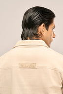 Close-up of man wearing beige corduroy jacket showing TZÁR logo back detail and ribbed texture.