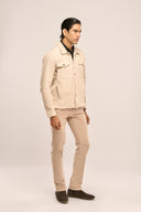 Man in beige corduroy jacket with flap & jetted pockets, metal buttons, beige pants, and dark brown boots, side profile view.