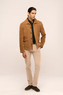 Man wearing brown suede leather jacket with full sleeves, horn buttons, spacious flap pockets, paired with beige pants.