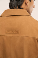 Back view close-up of man in brown suede leather jacket featuring collar and ​​TZÁR logo patch.
