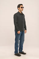 A man wearing a charcoal black cotton chambray shirt with jetted pocket and full sleeves, paired with jeans, side angle.