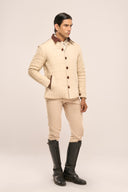 Man in beige quilted jacket with rust red buttons, collar & pocket detail, beige pants, and black boots, side profile view.