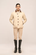 Man wearing a beige quilted jacket featuring rust red collar, buttons & pocket detail, beige pants, and black boots.