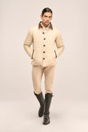 Man dressed in a beige quilted jacket with rust red accents, paired with beige trousers and black riding boots.