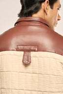 Close-up of a beige quilted jacket featuring a rust red leather yoke and collar with TZÁR logo detailing.
