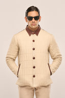 Man wearing a beige quilted jacket with rust red collar, buttons & pocket detail, paired with beige pants and sunglasses.