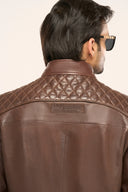 Close-up back view of man wearing coffee brown soft leather jacket with quilted shoulder detail and TZÁR logo patch.