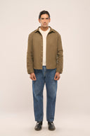 Man wearing olive color men’s shirt jacket featuring full sleeves & front pocket, white t-shirt, blue jeans, and black boots.