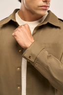 Close-up of man wearing olive color men’s shirt jacket featuring full sleeves, front pocket, and gold snap buttons.