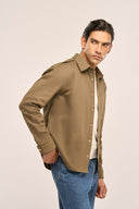 Man wearing an olive colour men's shacket featuring full sleeves, gold tone snap buttons, paired with jeans, side view.