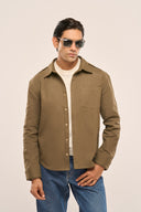 Man in sunglasses wearing an olive men's shacket with dropped shoulders, gold snaps, and full sleeves, paired with blue jeans.